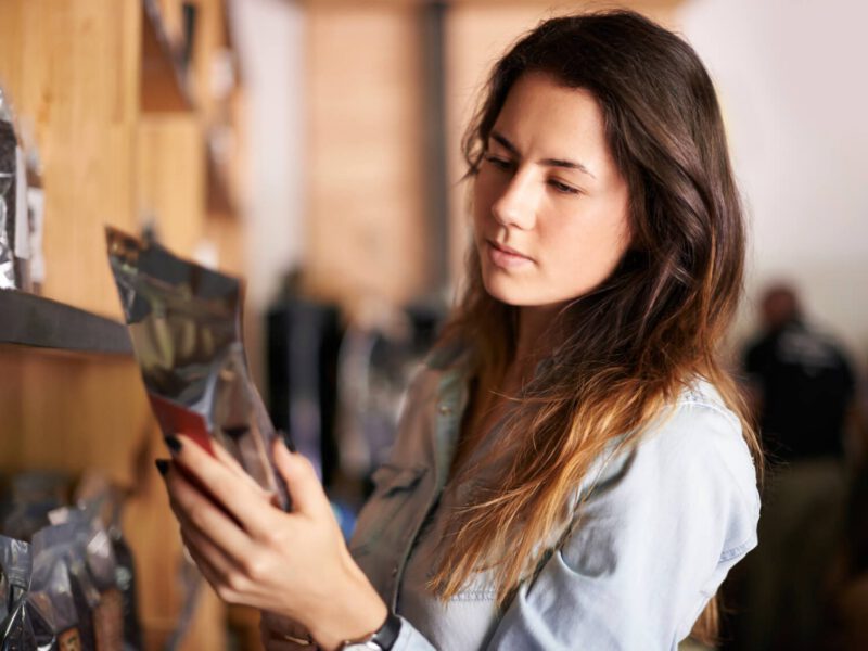 A woman examines the back of a package of food, studying the nutrition facts label