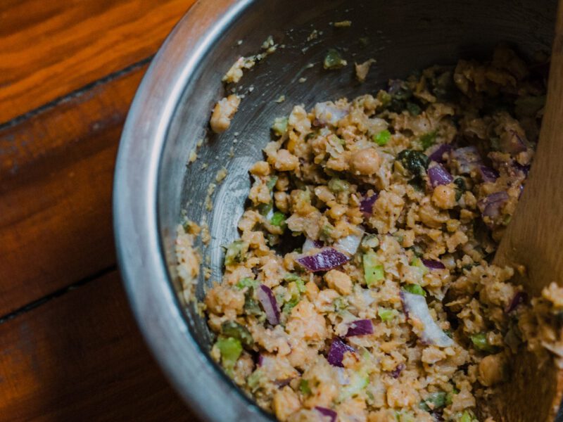 A dark grey ceramic bowl of vegan tuna salad with a small wooden spoon in the bowl