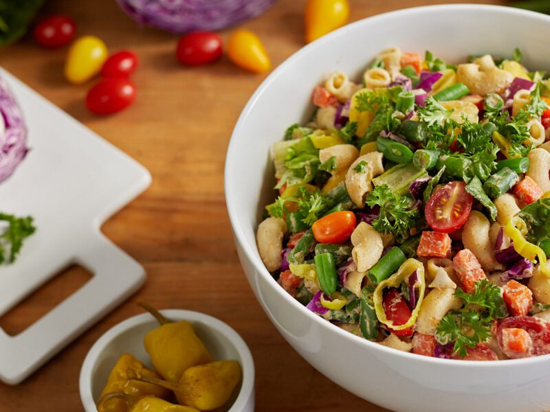 Chopped Veggie Salad with Pasta and Creamy Cauliflower Dressing in a white bowl with fresh veggies in the background