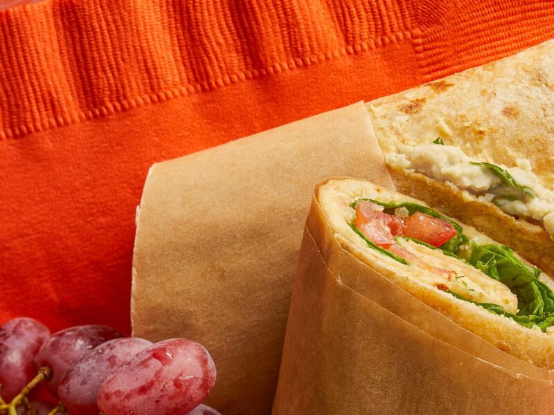 Quick Hummus and Quinoa Wrap wrapped in baking paper and cut in half on to of a bright orange paper napkin