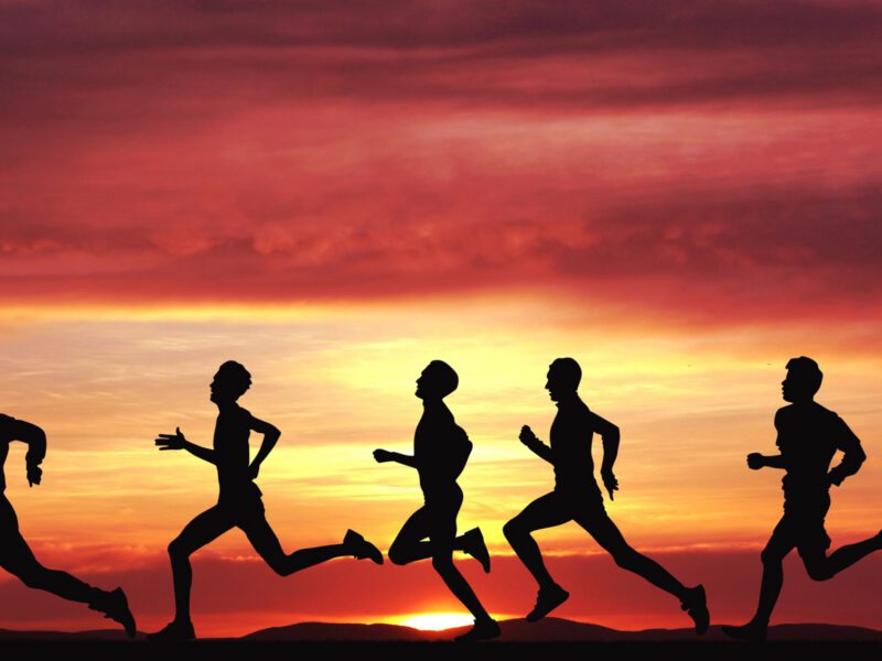 Silhouettes of men running against a sunset