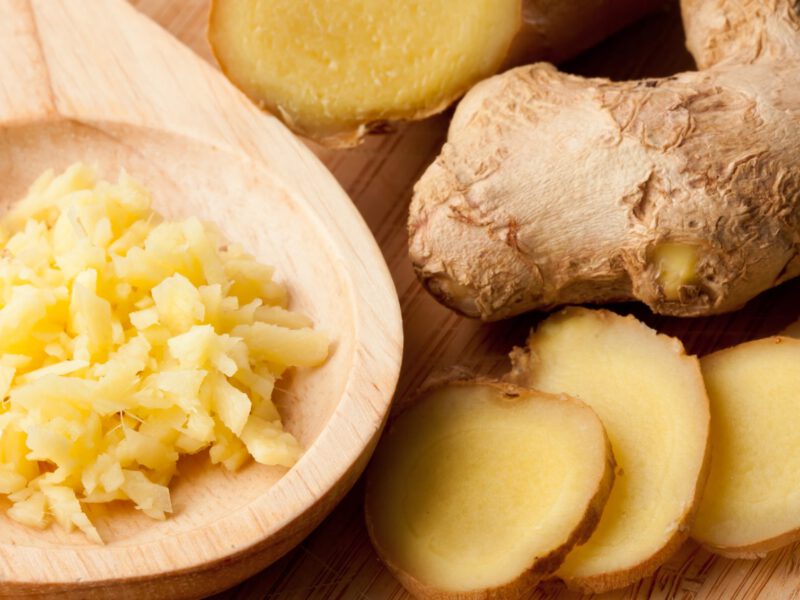 A whole root of fresh ginger next to slices of ginger and a wooden spoon of grated ginger