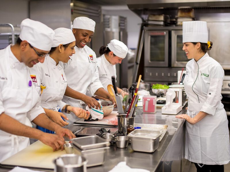 Chefs in white chef coats and hats smiled and laugh in a commercial kitchen