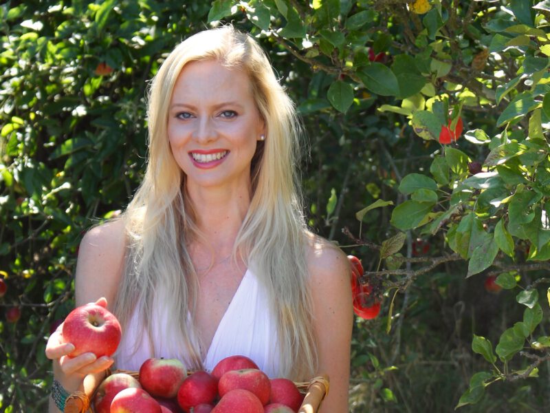 A smiling Lida van der Byl-Knoefel next to an apple tree holding a basket of apples