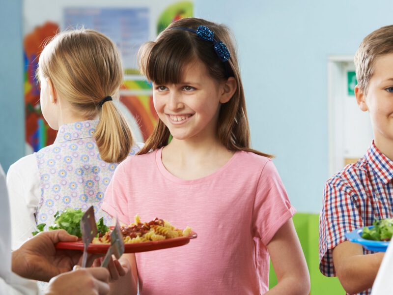Smiling elementary children receive a healthy plant-based school lunch