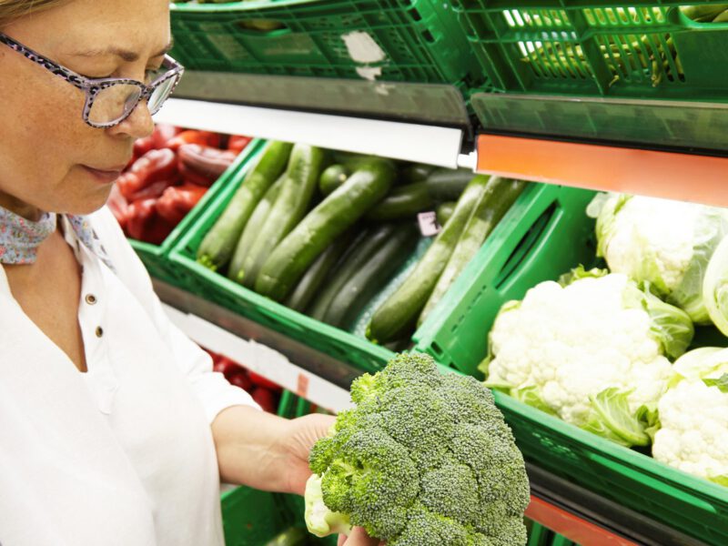 Woman looking at a head broccoli in the supermarket