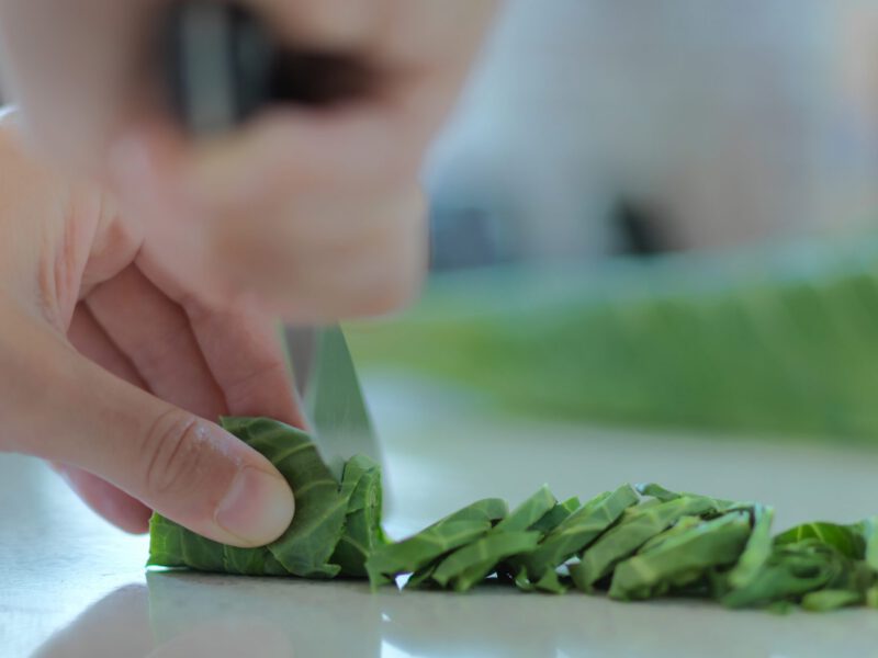 Close up shot of a person cutting rolled collard green thinly