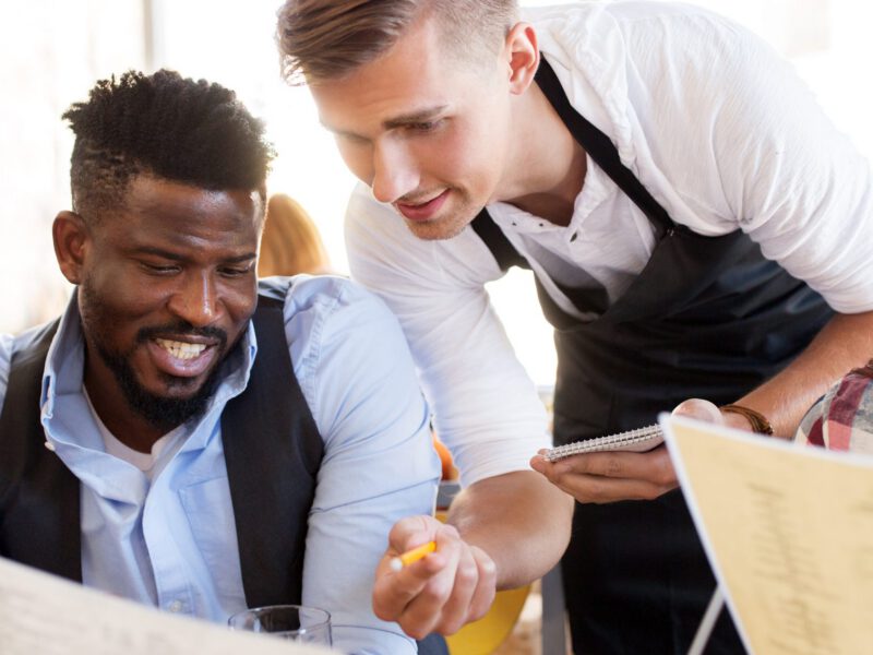 A young man and a woman at a restaurant, the man is talking to waiter, asking about the menu