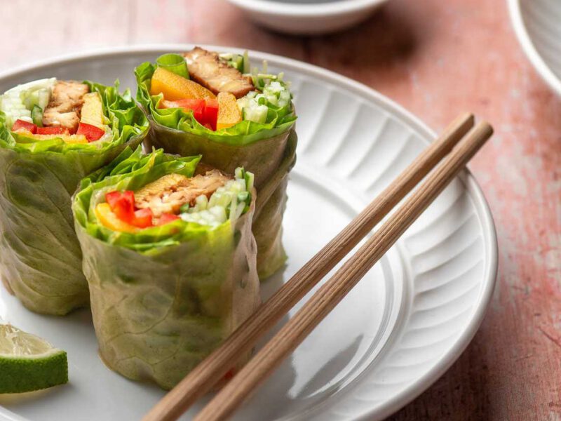 Spicy Tempeh Mango Spring Roll, cut in half, on a plate with chopsticks and a wedge of lime