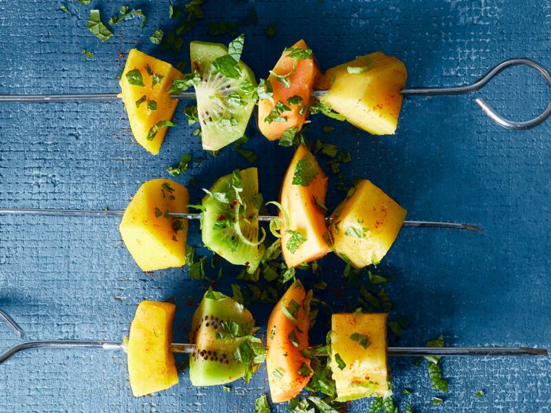 Three colorful Thai Fruit Skewers with Coconut and Lime against a blue background