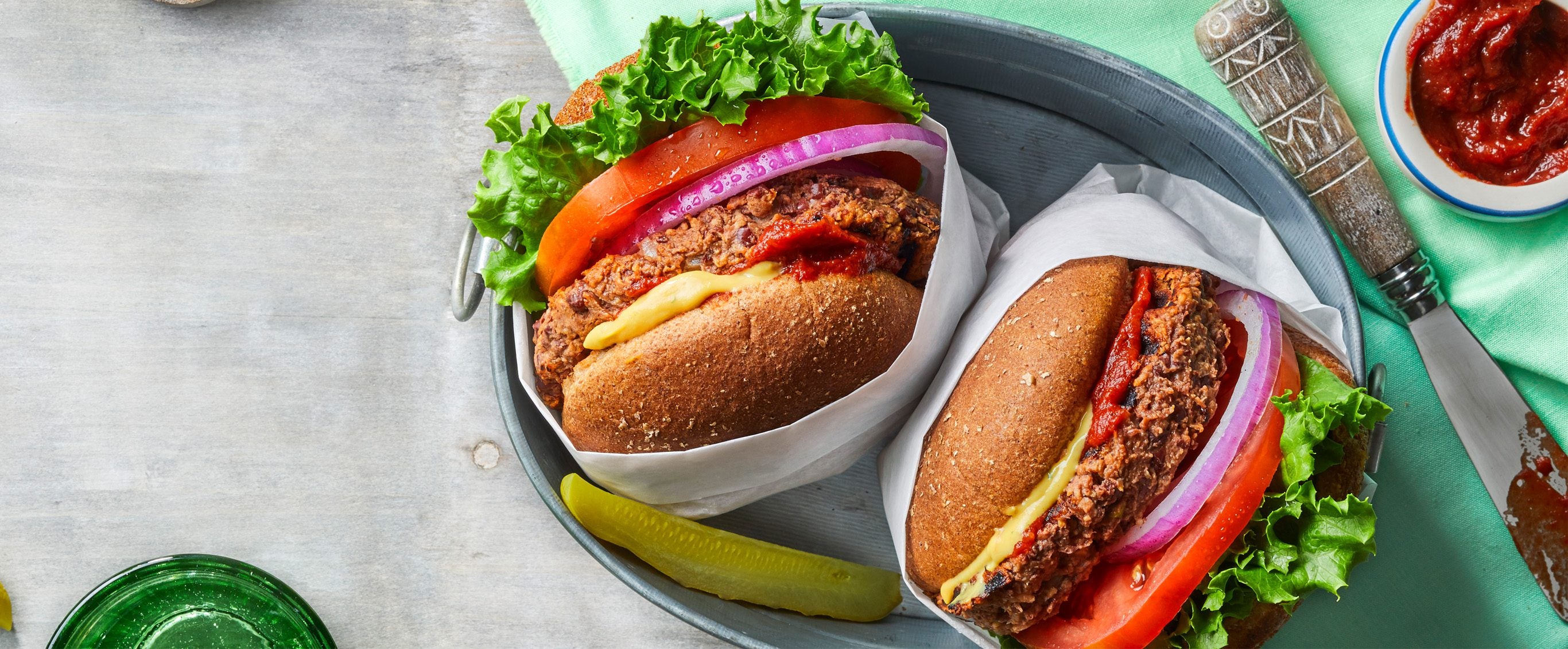 Two vegan five-ingredient veggie burgers with homemade patties and vegan cheese and slices of onion and tomato, shown from the side, in wrappers