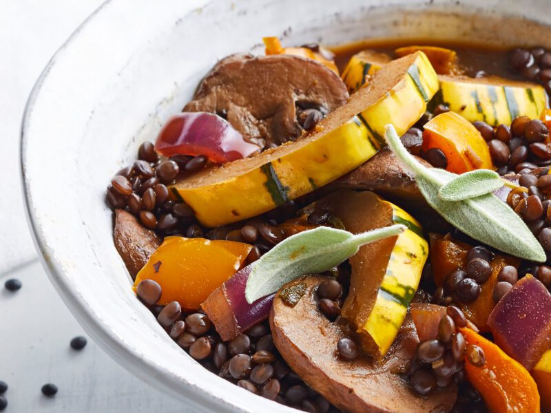 Sage Lentil Stew with Squash and Mushrooms in a rustic white bowl against a white background