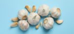 Six heads of garlic on a blue background with cloves beside them