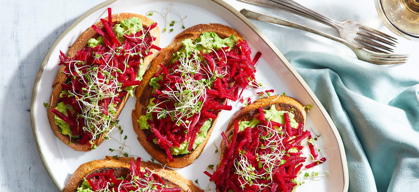 Vegan tartines - toast topped with avocado and bright beets and seasoned with ginger and wasabi, shown on a white plate