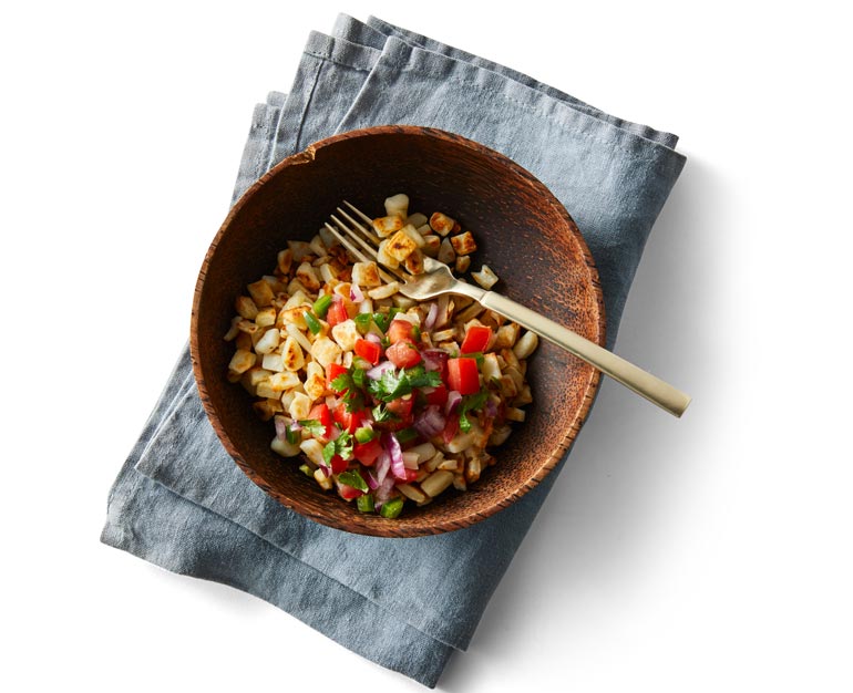 Hashbrowns in a wooden bowl on a gray napkin with a gold metal fork 