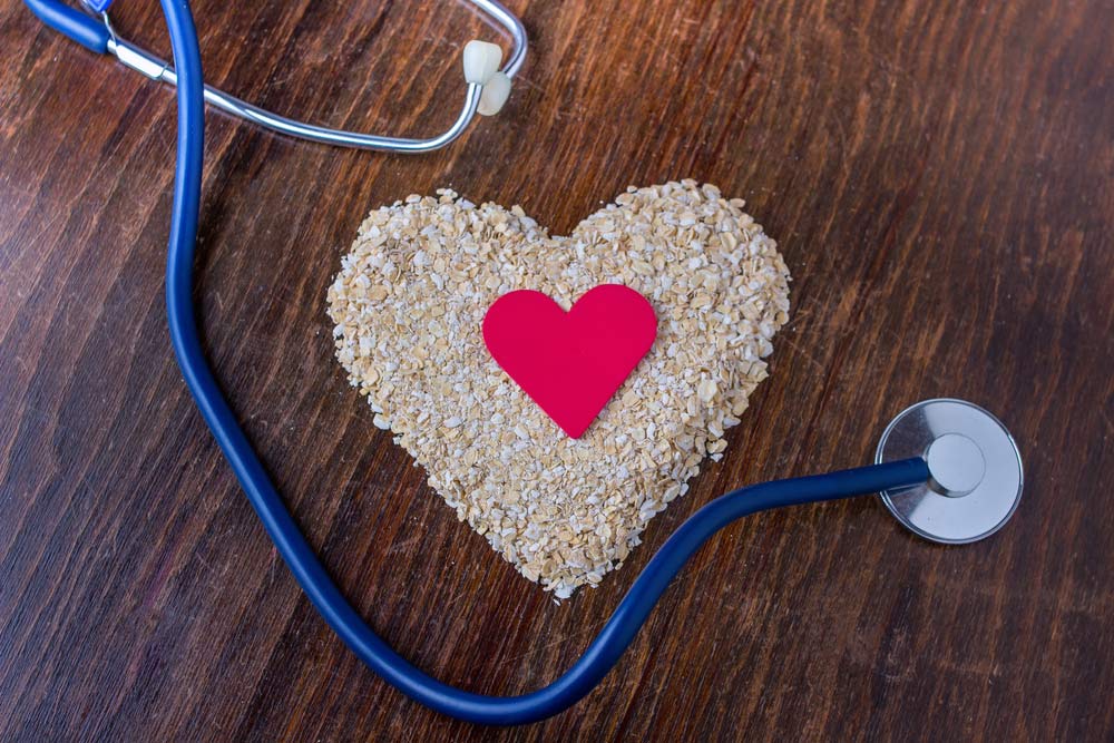 Oats shaped into a heart, with a smaller red heart at the center, beside a stethoscope on a wooden table