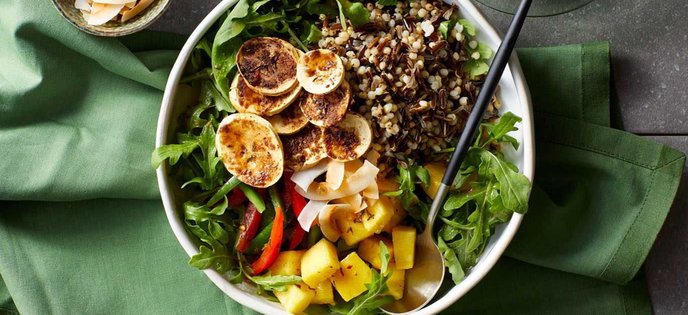 Colorful grain bowls with greens and sliced, crispy plantain chips, seasoned with jerk spices