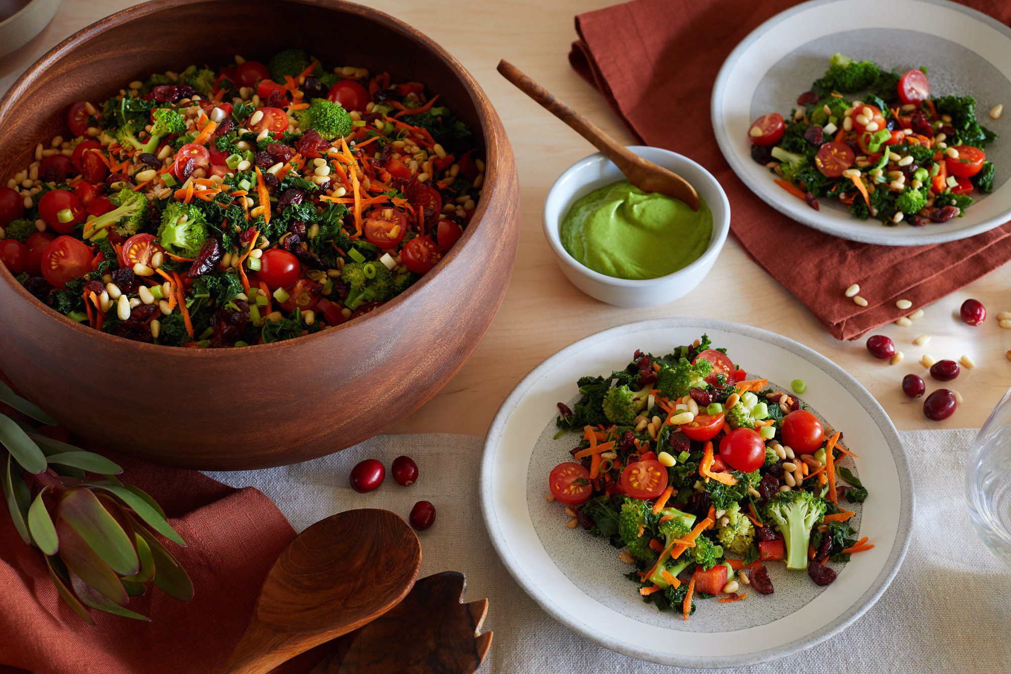 A large bowl of kale salad set alongside a plate with kale salad and a bowl with green avocado dressing