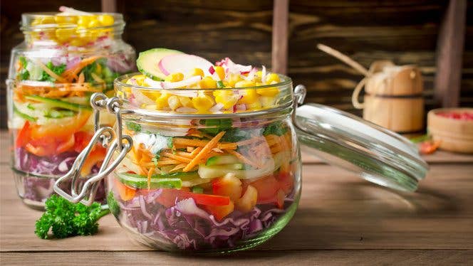 Clear glass jar with a salad in it on a wood countertop