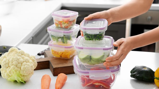 Hands stack clear Tupperware containers on top of each other that contain chopped veggies