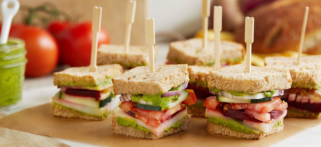 Stacked veggie sandwiches on a cutting board with wood toothpicks holding them together