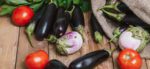 an array of nightshade vegetables -- including eggplant, tomato -- on a wooden table