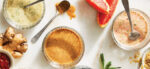 An array of homemade salad dressings made without oil, including vegan ranch, balsamic vinaigrette, and a grapefruit tarragon, in small glass bowls with spoons in them and some of the ingredients shown beside them