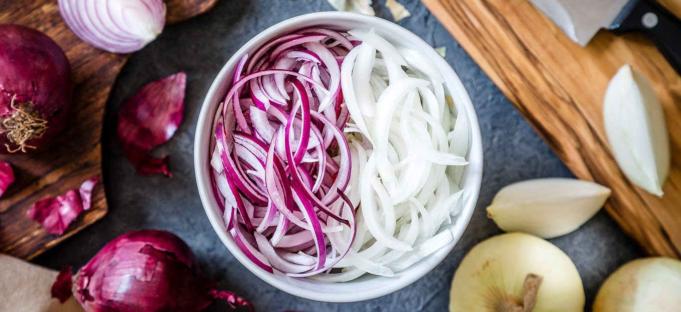 Bowl of sliced red and white onions, with whole red and white onions off to the side