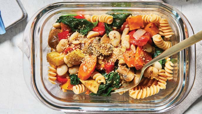 Italian Veggies and Pasta in a glass tupperware with a metal spoon