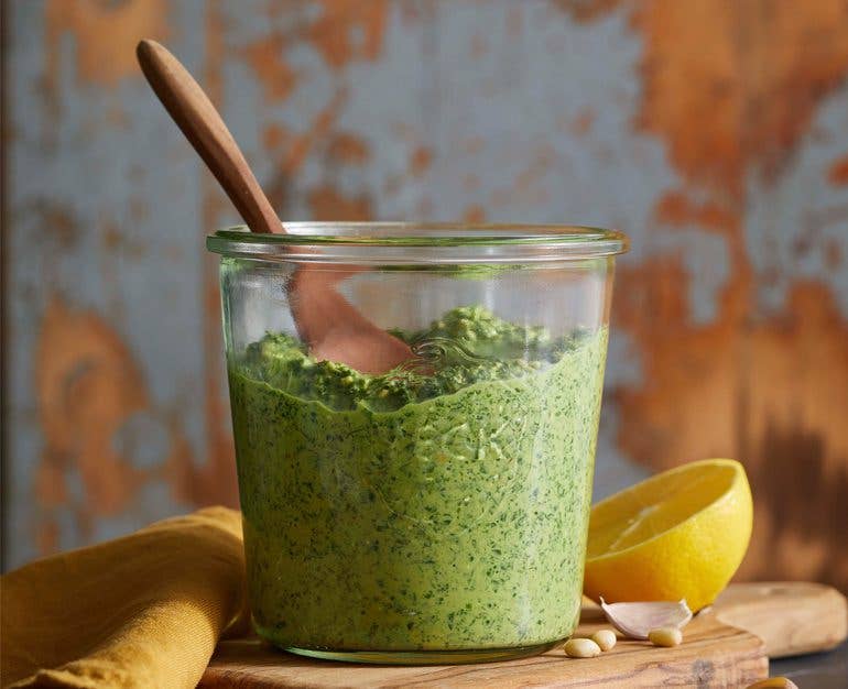 carrot top pesto in a glass jar with a wooden spoon