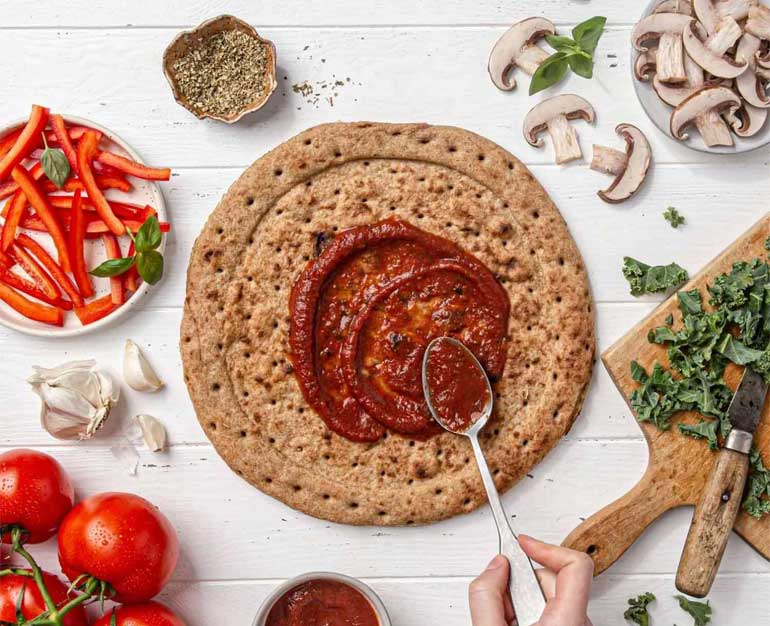Plantstrong pizza crust with a swirl of pizza sauce in the middle surrounded by fresh veggies