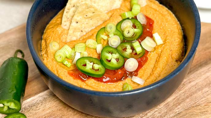Dark gray bowl full of vegan queso dip topped with salsa and jalapenos