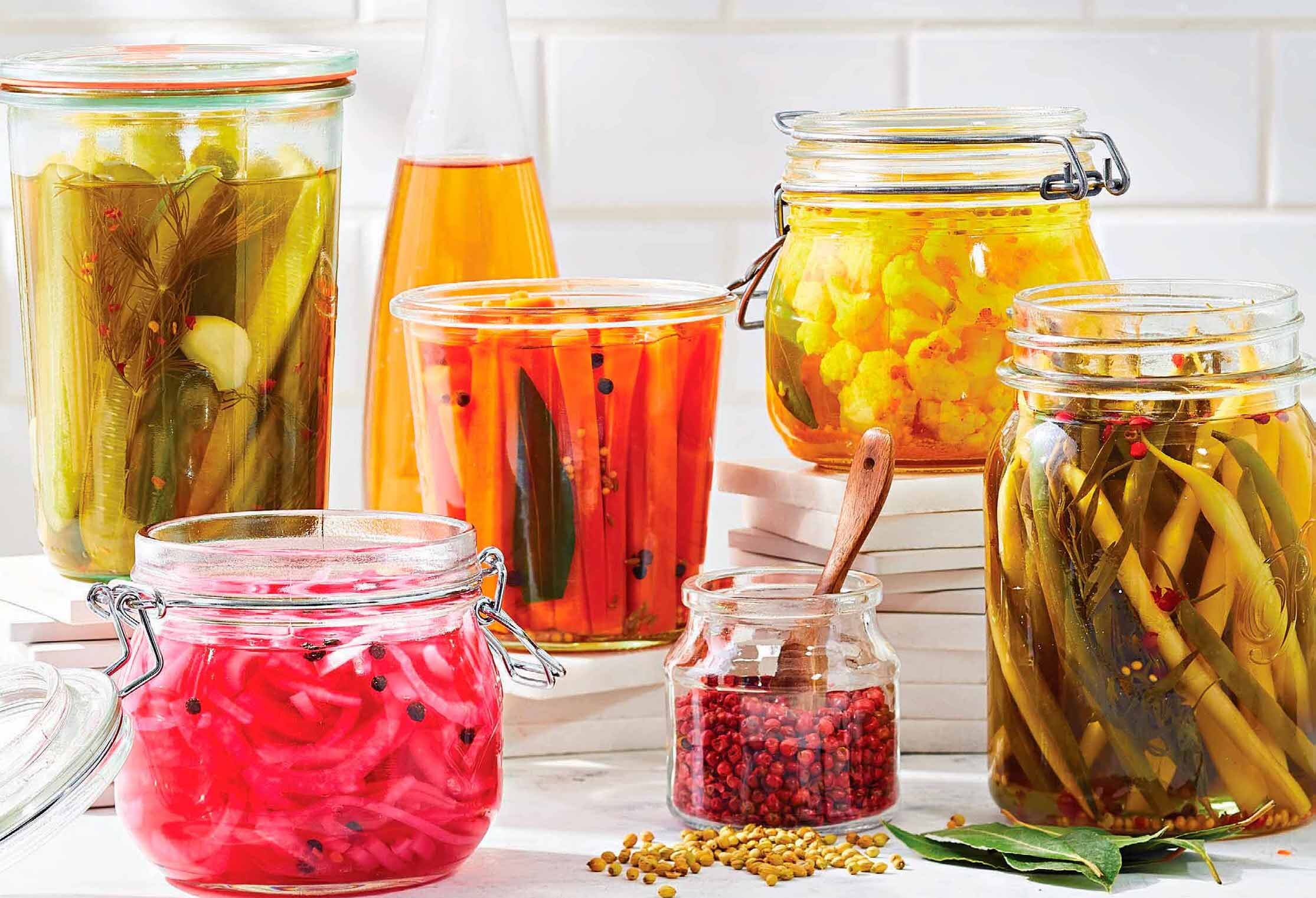 An array of different low-sodium quick-pickled vegetables, including pickles, carrots, quick-pickled red onions, and more, with a cruet full of vinegar in the background