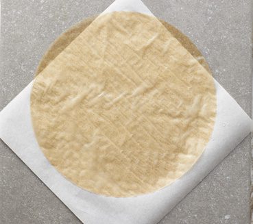 A circular sheet of brown rice paper laid over a white square of parchment paper