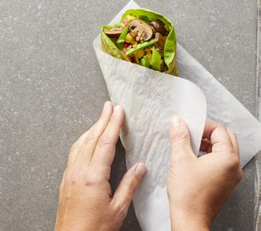 a hand wrapping parchment paper around a rice paper cone with mushrooms and veggies