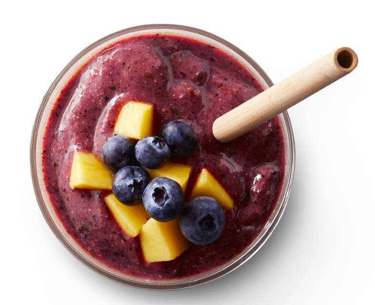 Purple smoothie with mango and blueberries on top and a wooden straw