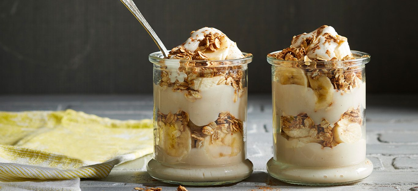 Two vegan banana pudding parfaits in glass jars, showing layers of pudding and vanilla oats