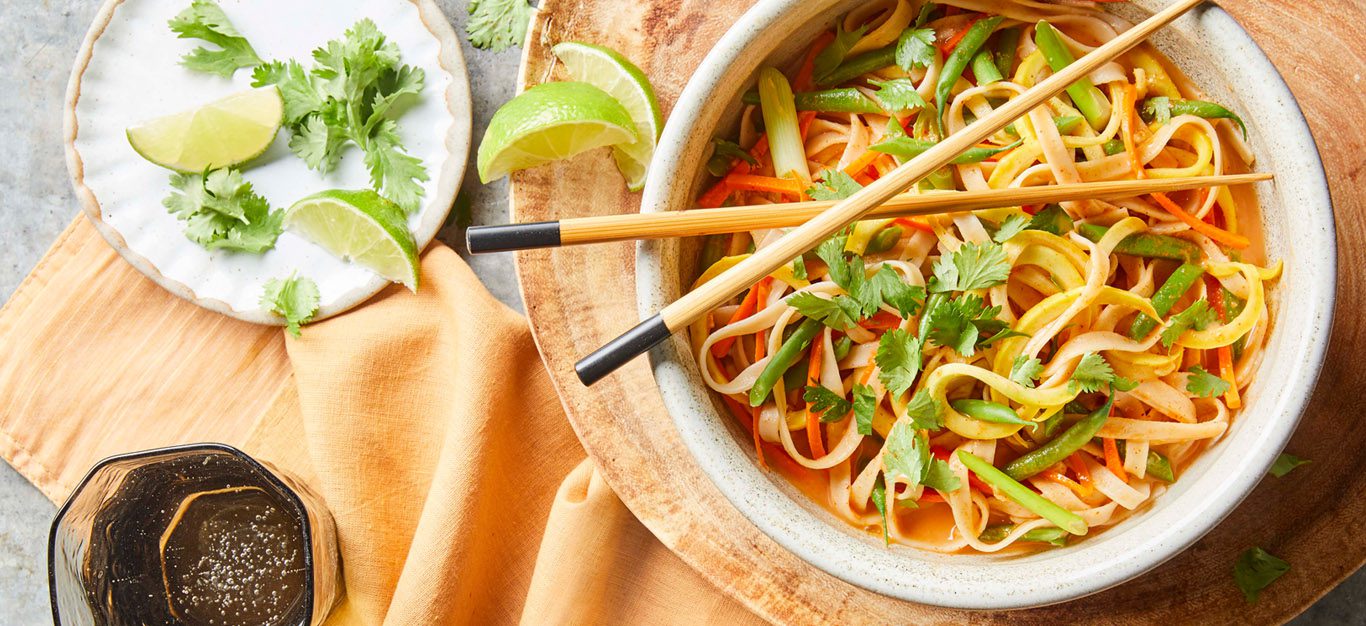spicy curried thai noodle bowls with chopsticks on a decorative wooden plate