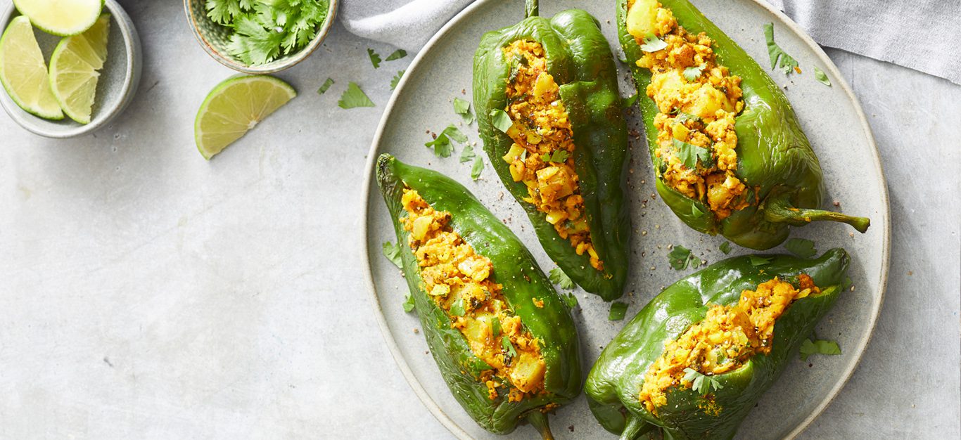 Vegan Indian-Spiced Stuffed Poblano Peppers - Four stuffed green poblano peppers on a white plate and white table