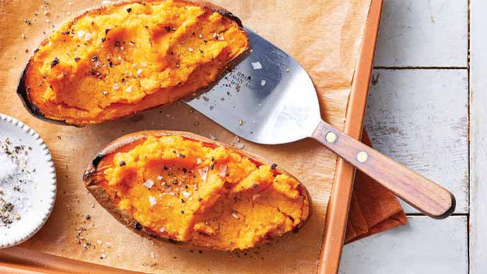 Sriracha Stuffed Sweet Potatoes on a parchment lined baking sheet with a metal spatula