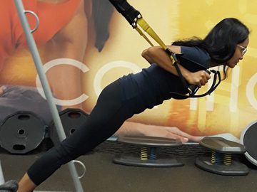 A young woman uses a trx machine to train at the gym