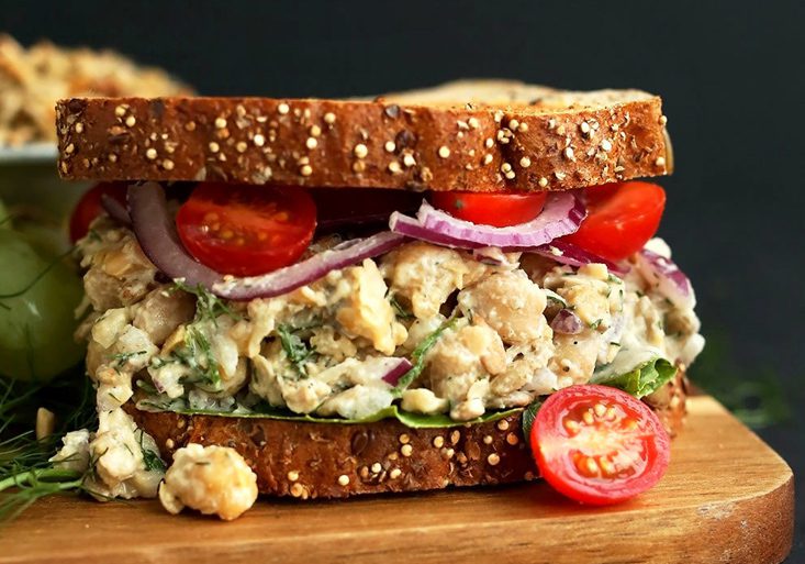 No Tuna Salad Sandwich - A Vegan Tuna Salad on Toasted Whole Grain Bread, Topped with Cherry Tomatoes and Sliced Red Onion, Served Beside Grapes on a Cutting Board
