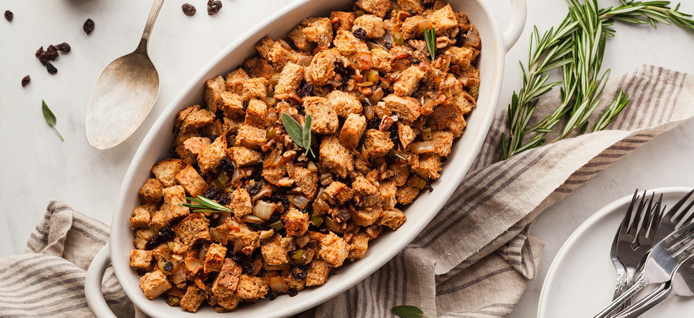 Vegan whole grain stuffing shown in white casserole dish, sprinkled with dried currants