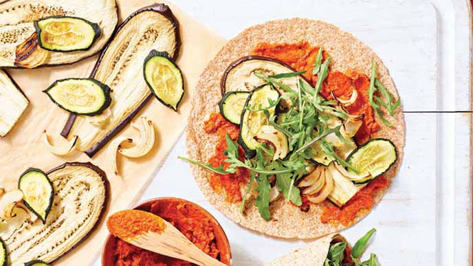 Roasted Veggie Wraps with Roasted Red Pepper Hummus Spread on white tiles next to sliced eggplants